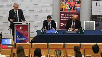 3 osoby przemawiają przed widownią na sali wykładowej.