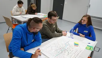 Three people sitting with project drawing on a desk.