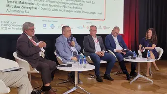 Pięć osób siedzi na scenie podczas konferencji. Rozmawiają przez mikrofon.