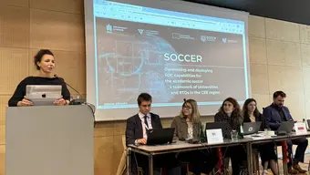 Grupa osób na sali wykładowej. W tle prezentacja o SOCCER