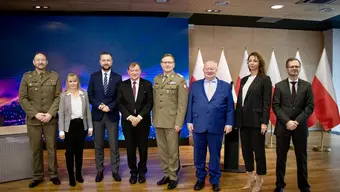 8 people standing in a conference room. Polish flag is behind them.
